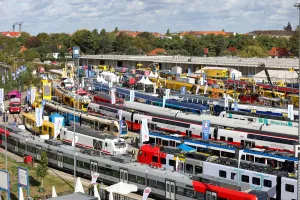 Colorful trains on display at an outdoor exhibition, with people walking between them.