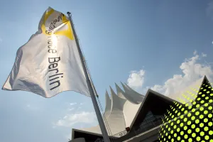 Weiße Fahne mit Berliner Schriftzug vor dem Tempodrom und blauem Himmel.