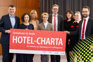 Acht Personen halten gemeinsam ein rotes Schild mit der Aufschrift „HOTEL-CHARTA“.