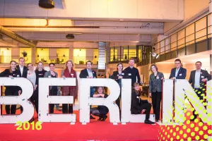 Gruppe von Menschen steht hinter großen BERLIN-Buchstaben auf rotem Teppich, drinnen.