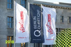 Drei Fahnen vor einem Gebäude, zwei mit Visit Berlin Logo, eine mit Berlin Questions.