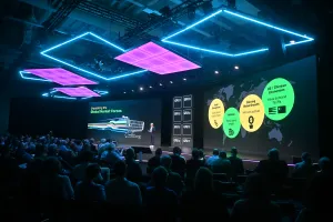 Speaker presenting on stage at a tech conference with colorful lights and audience watching.