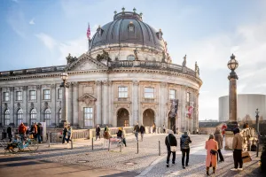 People walking in front of a domed historic building on a sunny day.