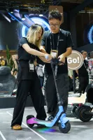 Two people examining a blue electric scooter at an indoor event.