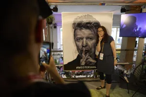 A woman poses next to a David Bowie poster.