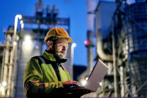 Young engineer wearing a helmet and using a laptop during his night shift. Engineering concept.