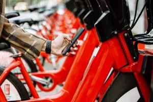 erson uses a smartphone to unlock a red rental bike at a bike-sharing station.