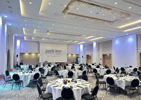 Banquet hall with round tables set for an event, white tablecloths, stage at front.
