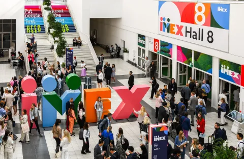 Crowd at a convention center entrance with large colorful IMEX letters and Hall 8 signage.
