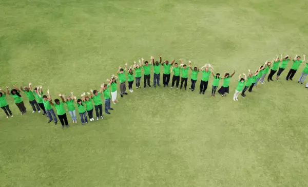 Portrait of people in green t-shirts forming wavy line in field