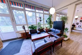 Heller Aufenthaltsraum mit modernen Sesseln, großem Fenster und Pflanzen.