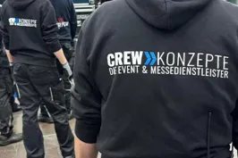 Zwei Crewmitglieder in schwarzen Hoodies mit Aufschrift, arbeiten an einer Veranstaltung.
