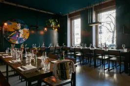 Modernes Restaurant mit gedeckten Tischen, großen Fenstern und dunkler Wandfarbe.