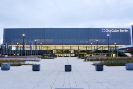 Moderne Glasfassade des CityCube Berlin bei Dämmerung, beleuchtet und umgeben von Parkplatz.