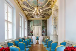 Prunkvoller Hochzeitssaal mit blauen Stühlen, Kronleuchter und bemalter Decke.