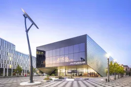 Modernes, kantiges Gebäude mit Glasfassade und großem Solarmodul auf dem Vorplatz