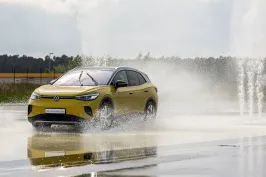 Gelbes Auto fährt durch große Wasserpfütze auf nasser Straße, Wasser spritzt hoch.