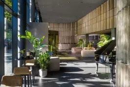 Heller Hotellobby mit großen Fenstern, Pflanzen, Sofas und einem schwarzen Flügel