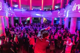 Menschenmenge auf einer Party mit bunter Beleuchtung und Musiker auf der Bühne.