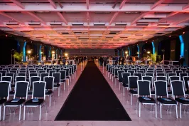 Großer Konferenzsaal mit vielen leeren Stuhlreihen und bunter Deckenbeleuchtung.