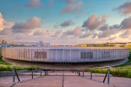 Rundes, modernes Gebäude bei Sonnenuntergang, vorne Treppen und Handlauf.