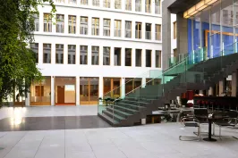 Modernes, helles Atrium mit Glastreppe und Tischen, große Fenster im Hintergrund.
