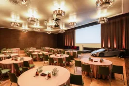 Konferenzraum mit runden Tischen, großer Leinwand und einem silbernen Auto auf der Bühne.