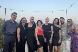 Acht Personen posieren lächelnd auf einer Terrasse bei Sonnenuntergang.