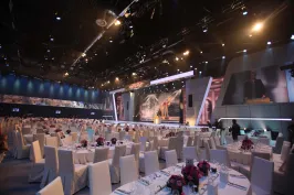 Großer, elegant dekorierter Veranstaltungssaal mit vielen runden Tischen und lila Blumen.