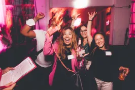 Vier fröhliche Menschen netzwerken in einem pink beleuchteten Raum.