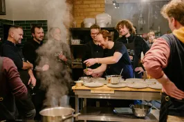 Gruppe von Menschen lacht und kocht gemeinsam in einer Küche.