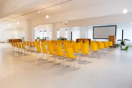 Heller Konferenzraum mit gelben Stühlen, Beamer und Leinwand.