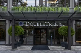 Hoteleingang mit DoubleTree by Hilton Logo, Glasdach und zwei großen Pflanzen.