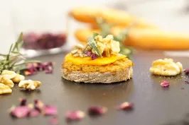 Rundstulle mit Aufstrich, Karotte und Walnuss auf schwarzem Teller, dekorativ angerichtet.