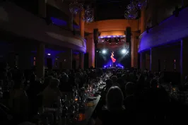 Dunkler Saal mit Publikum, Bühne beleuchtet, Artistin schwebt in der Luft.