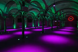 Gewölbekeller mit lila und grüner Beleuchtung, rotes VIP-Schild an der Wand.