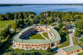 Modernes, ovales Gebäude mit begrüntem Dach am See, von Bäumen umgeben.