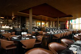 Modernes Restaurant mit braunen Ledersesseln und gedeckten Tischen, warm beleuchtet.