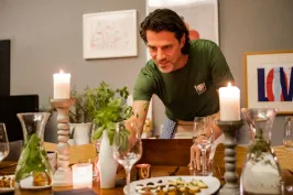 Mann deckt festlich gedeckten Tisch mit Kerzen und Speisen.