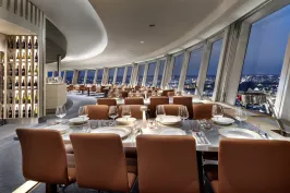 Modernes Restaurant mit gedeckten Tischen und Panoramablick auf die Stadt bei Nacht.