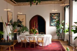 Stilvoll gedeckter Tisch in einem hellen Raum mit Pflanzen und Kunstwerken an den Wänden.