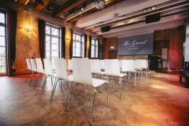 Heller Konferenzraum mit weißen Stühlen, Leinwand und großen Fenstern