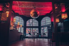 Moderne Bar mit großen Fenstern, roten Lichtern und einer silbernen Discokugel an der Decke.