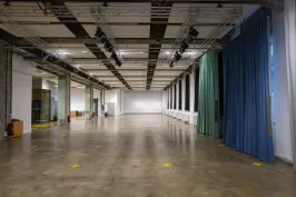 Leere Veranstaltungshalle mit Betonboden, Vorhängen und Deckenbeleuchtung.