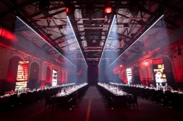 Langer Festsaal mit zwei gedeckten Tafeln, rote Beleuchtung, industrielle Atmosphäre.