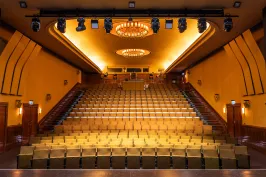 Leerer Kinosaal mit gelben Sitzen und zwei Kronleuchtern an der Decke.