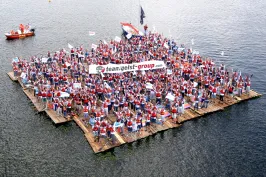 Große Menschenmenge auf Floß, hält Banner, schwimmt auf See.