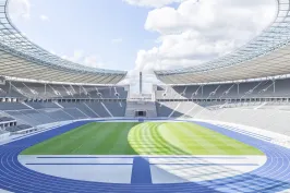 Innenraum des Olympiastadions Berlin mit Tribünen, blauer Laufbahn und grünem Fußballrasen