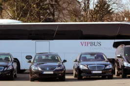 Mehrere schwarze Limousinen und ein großer VIP-Reisebus auf einem Parkplatz.