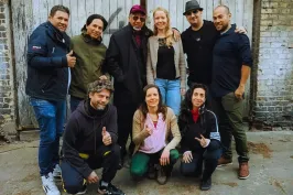 Neun lächelnde Menschen posieren vor einer alten Holztür auf einem Hinterhof.